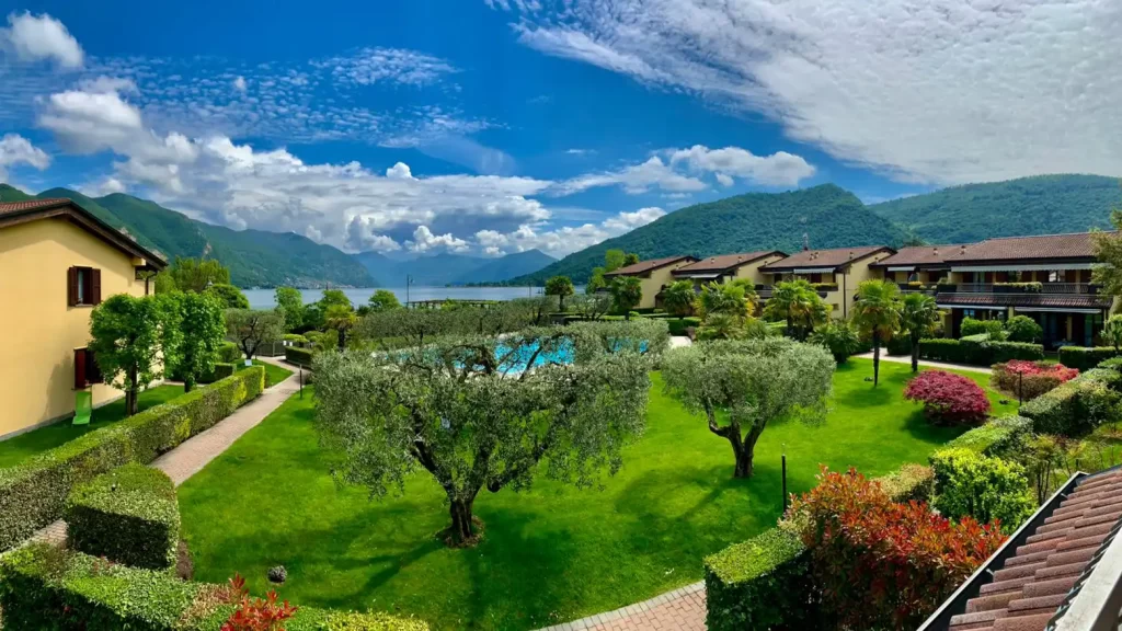 Giardino curato con alberi e arbusti fioriti affacciato su un lago circondato da montagne.