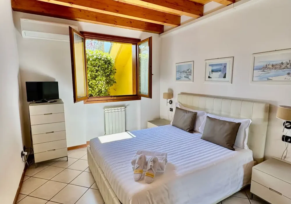 Camera da letto moderna e luminosa con letto matrimoniale, travi a vista e finestra aperta.