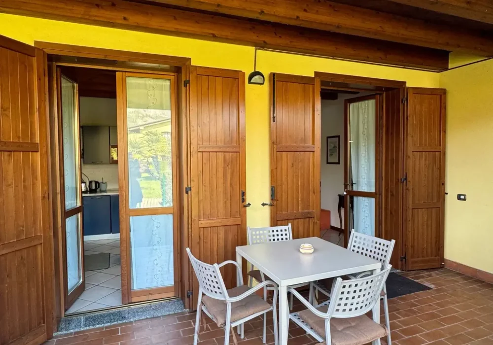 Terrazza con tavolo e sedie di fronte a porte in legno aperte.
