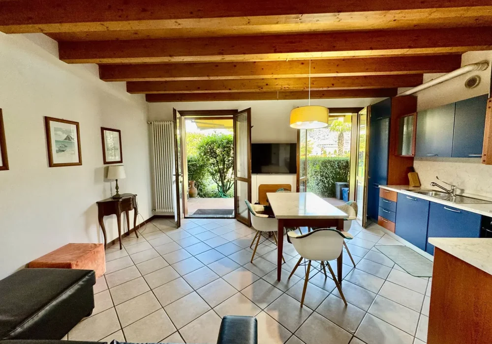 Soggiorno luminoso con tavolo da pranzo, cucina moderna e porte che si aprono su un giardino.