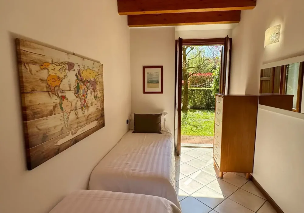 Camera da letto a due letti con travi a vista e una porta finestra aperta sul giardino.