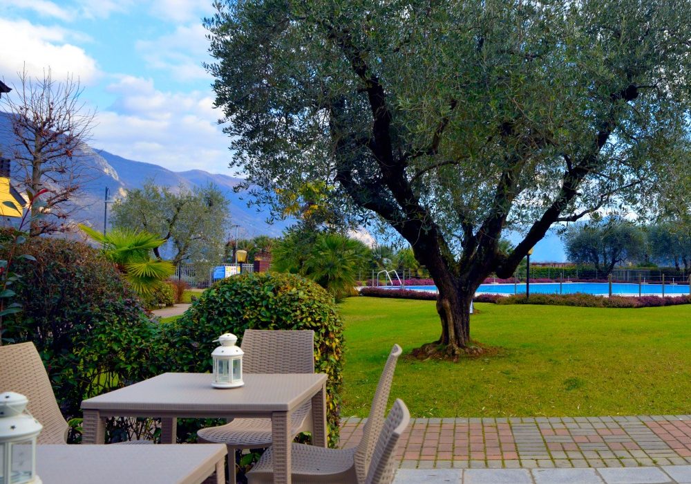 Terrazza arredata con vista su giardino e alberi, sotto un cielo sereno.